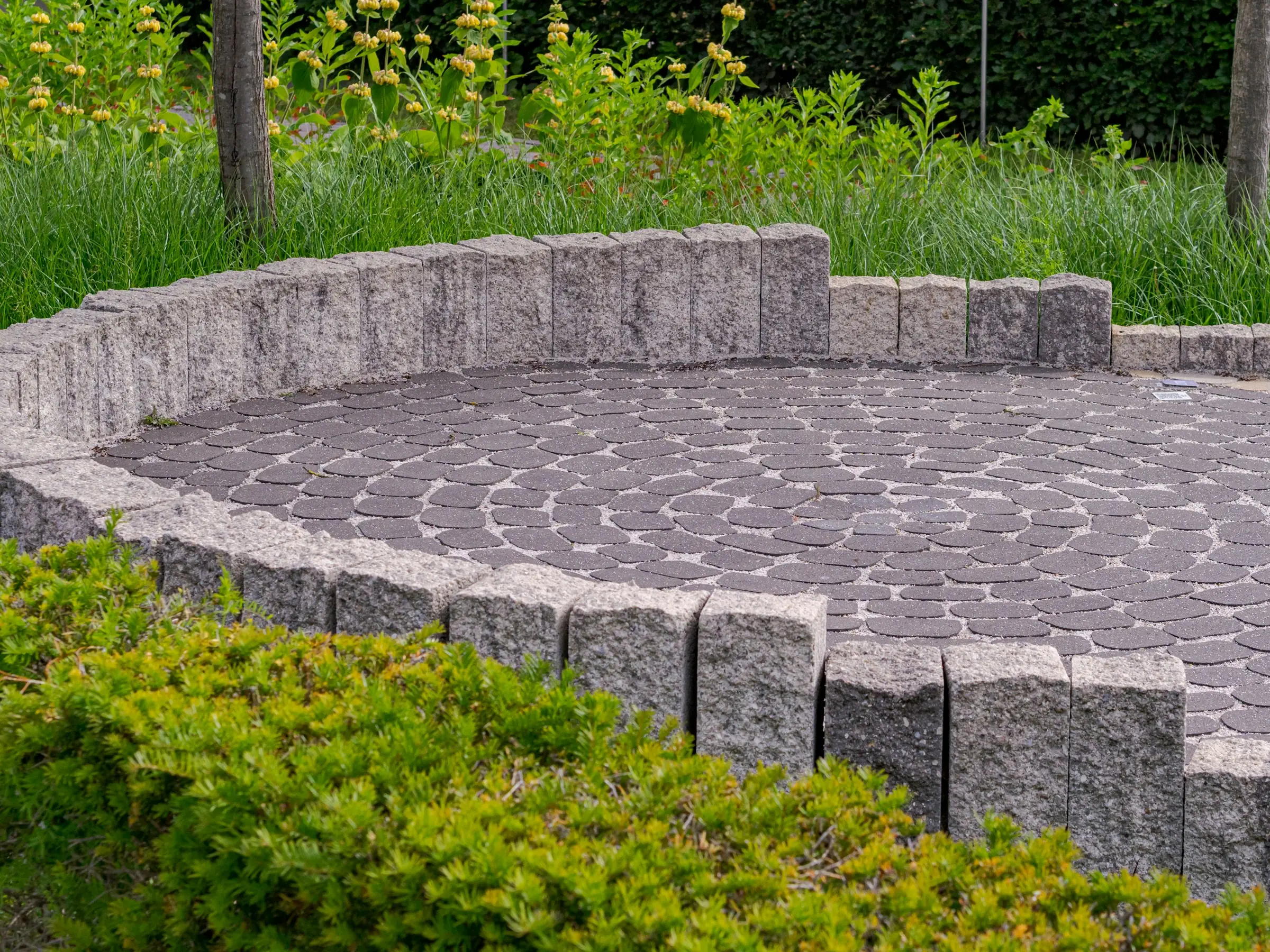Circular paver patio framed by a block seat wall and green shrubs